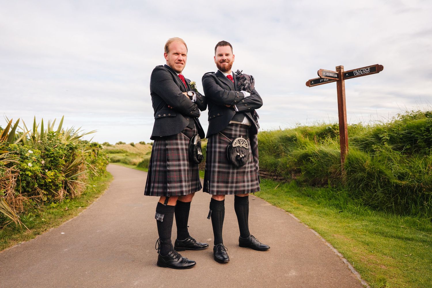 Wedding party members stand near a wooden cross on a hilltop path. Portmarnock Hotel Wedding PHOTOGRAPHER Dublin