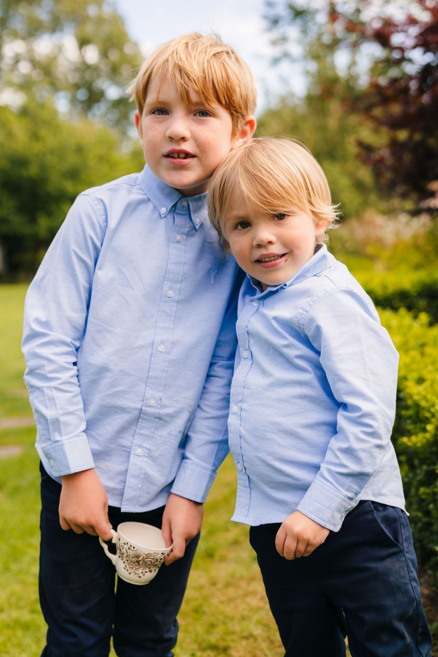 Two children in matching light blue shirts and dark pants play together on a sunny day in a grassy field. . Village Barn Tyrrellspass weddin