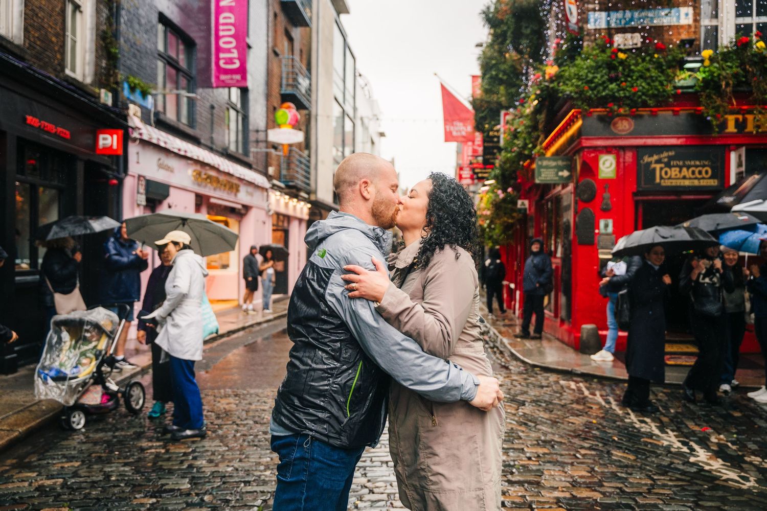 Proposal Dublin Rain falls on a busy cobblestone street in Edinburgh's historic Old Town as pedestrians with umbrellas walk past shops.