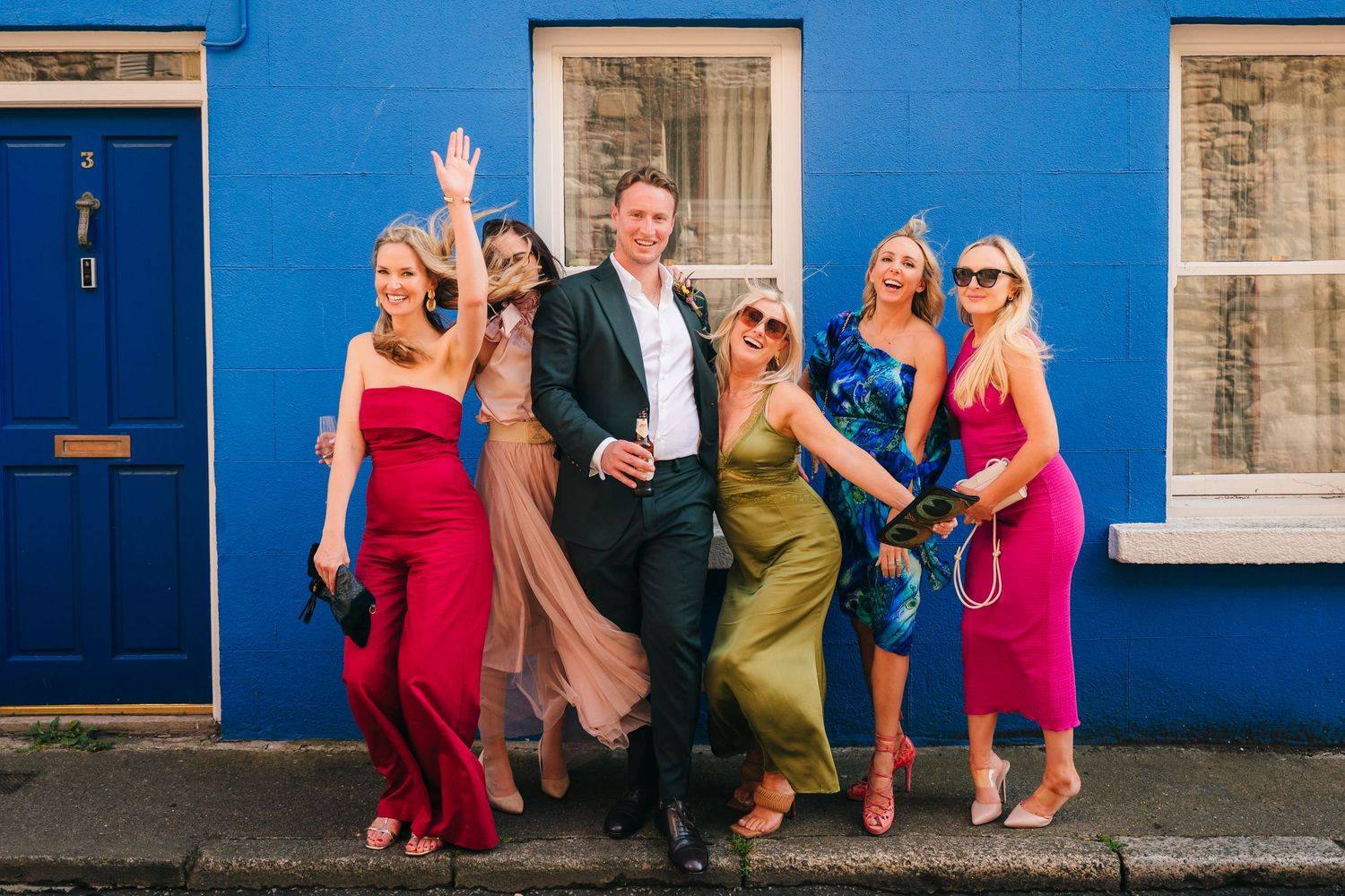 Group photo of wedding guests posing against a bright blue wall. Same sex wedding PHOTOGRAPHER Dublin