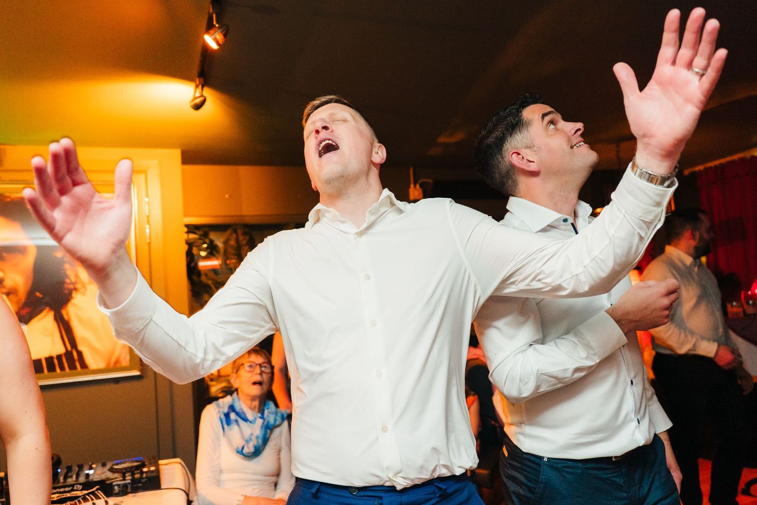 Party guests dance enthusiastically with arms raised at a lively indoor celebration. Marco Pierre Dublin Wedding Photographer