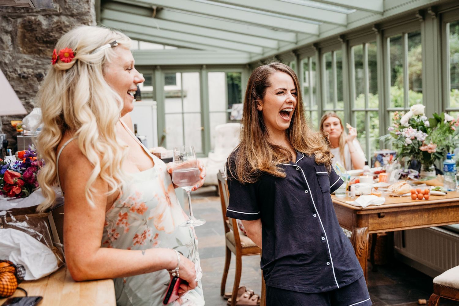 Two women laugh joyfully during an outdoor gathering with food and drinks at a patio restaurant. Wedding photographer Dublin