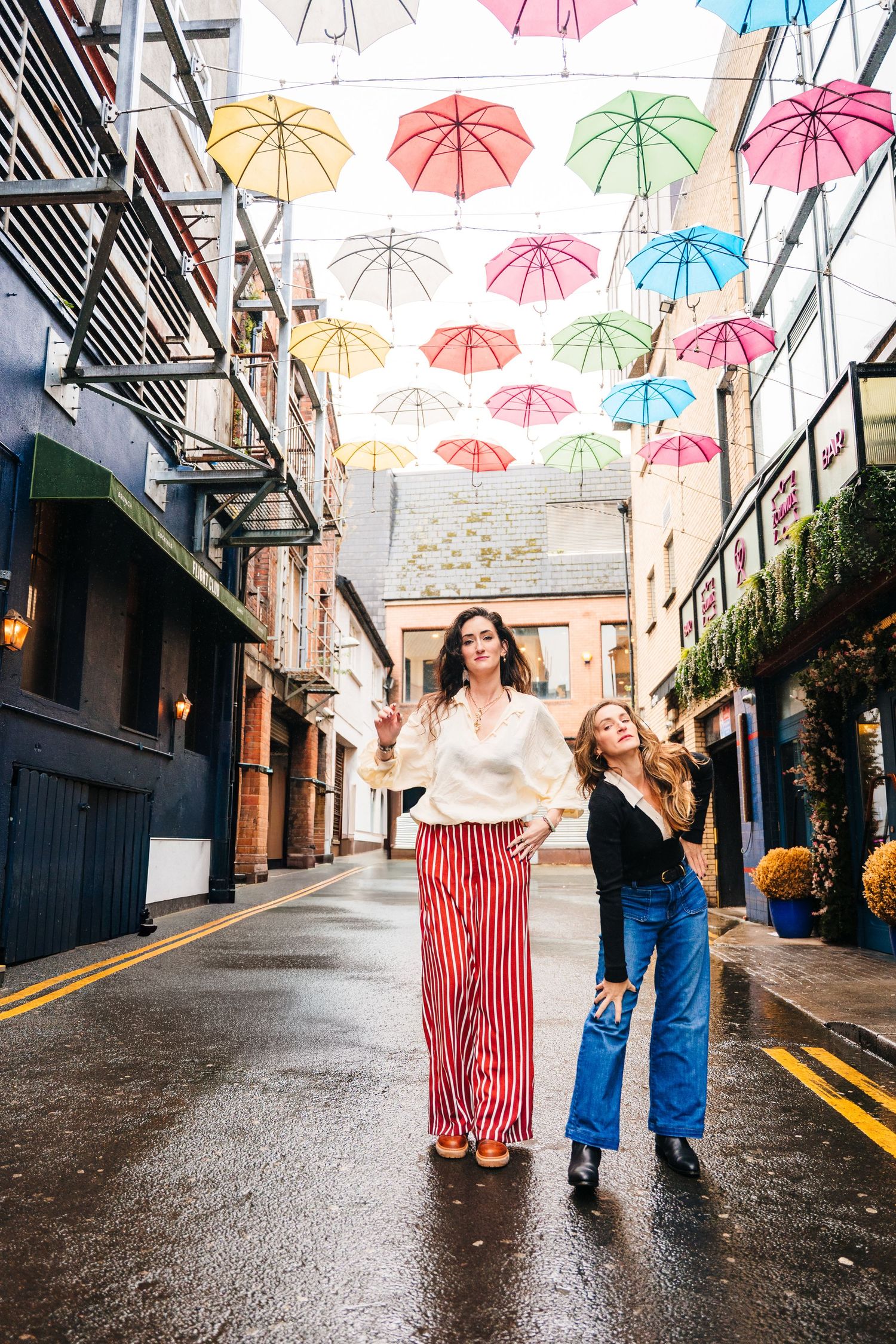 Colorful umbrellas hang above a wet cobblestone street while people walk beneath on a rainy day. professional headshots dublin photographer