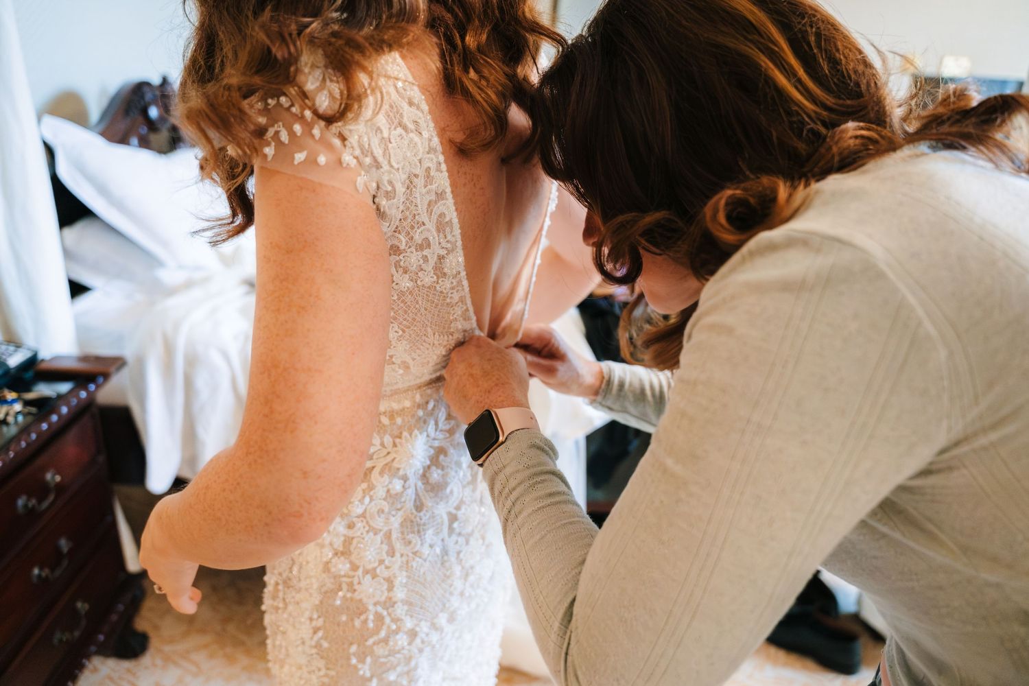 Wedding party getting ready with final dress adjustments and preparations in an elegant room.