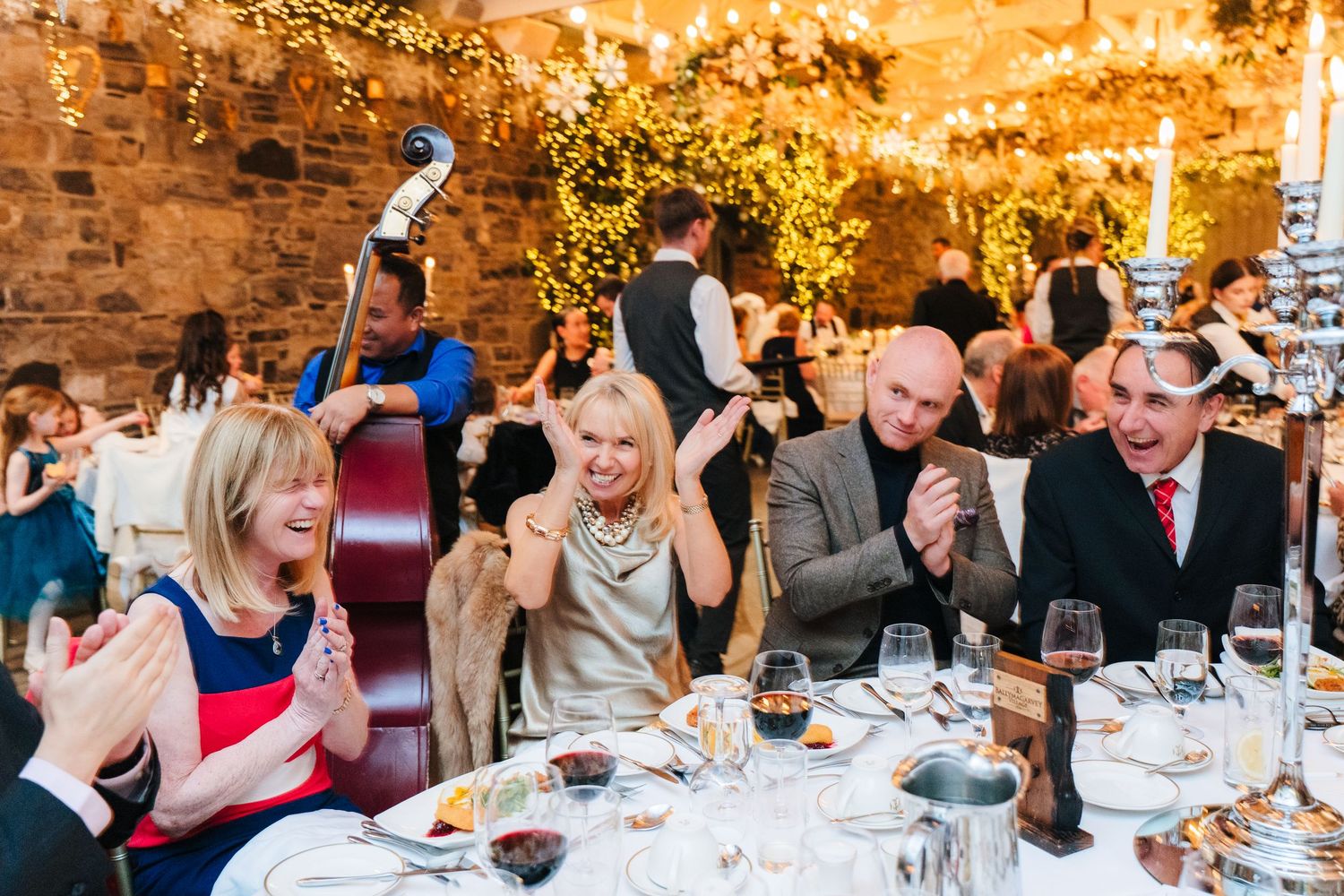 Wedding reception guests laugh and socialize while seated at elegant tables with glowing candlelight. Ballymagarvey Wedding photographer