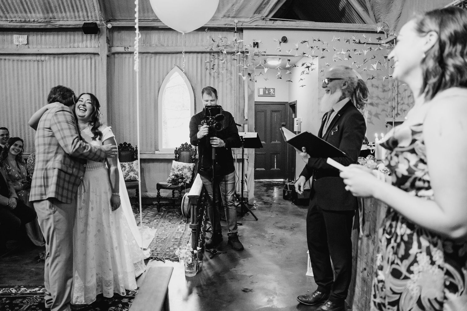 A couple embraces during their wedding ceremony while guests observe in a rustic venue. Wedding photographer Dublin