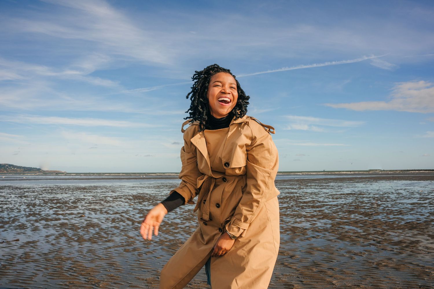 Dynamic beach fashion photography with a flowing beige coat against the shoreline. Dublin professional headshot photographer