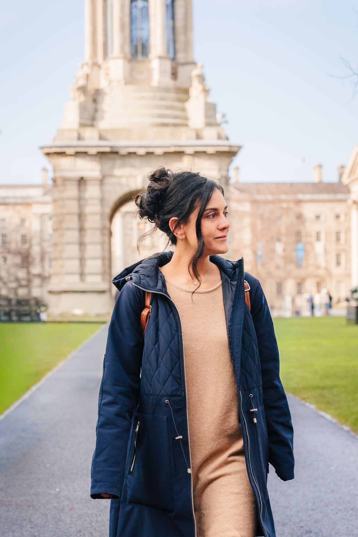 A person in a navy coat stands on a path with a grand historic building visible in the background. professional headshots dublin