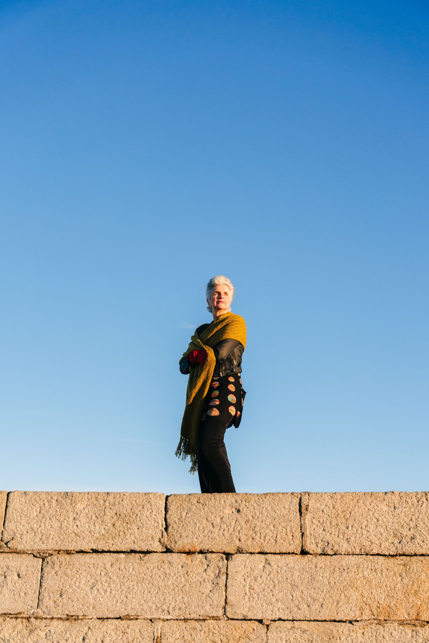 A silhouetted figure in yellow scarf stands atop a concrete wall against bright blue sky. professional headshots branding photographer dubli