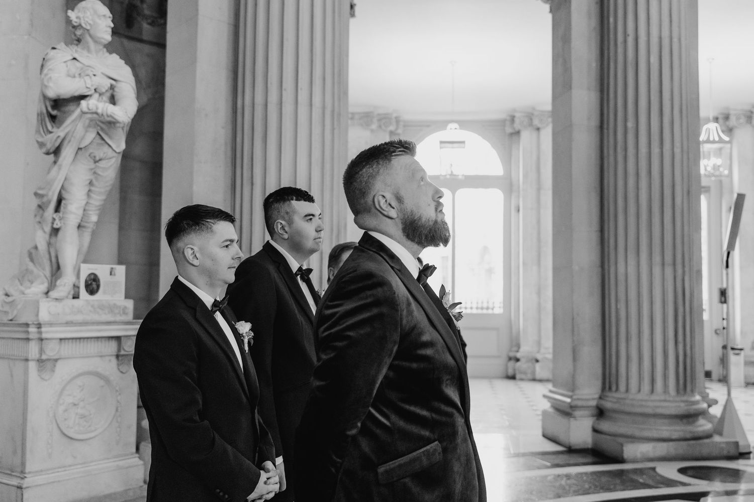Groomsmen standing in elegant venue with classical columns and statues. Wedding photographer dublin