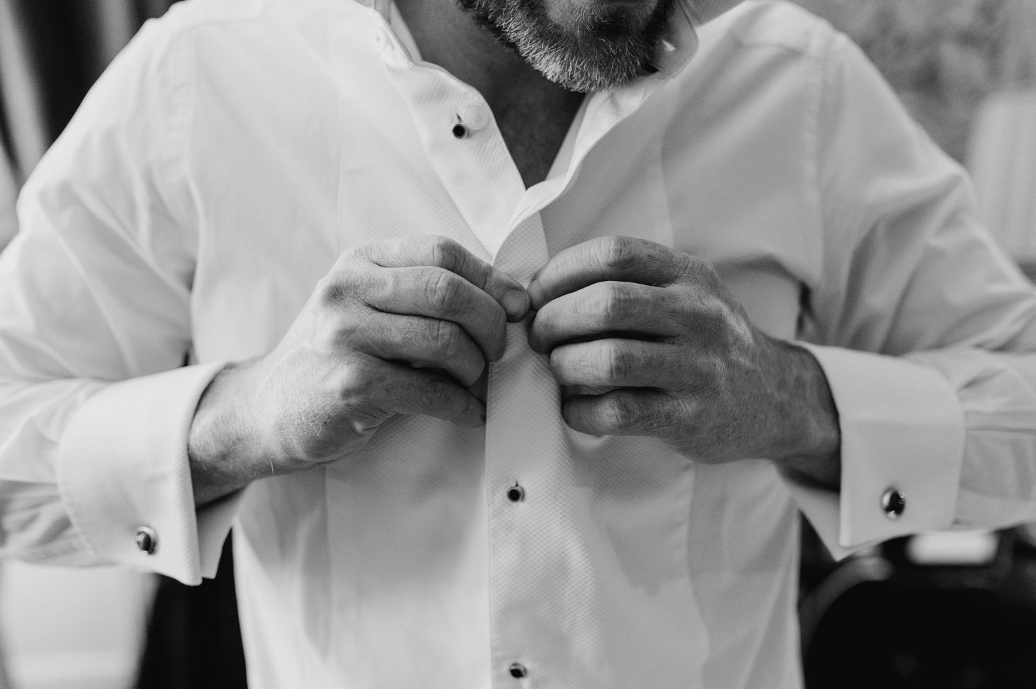 Close-up black and white photo of hands adjusting buttons on a white dress shirt. Castle Leslie Wedding Photographer Dublin