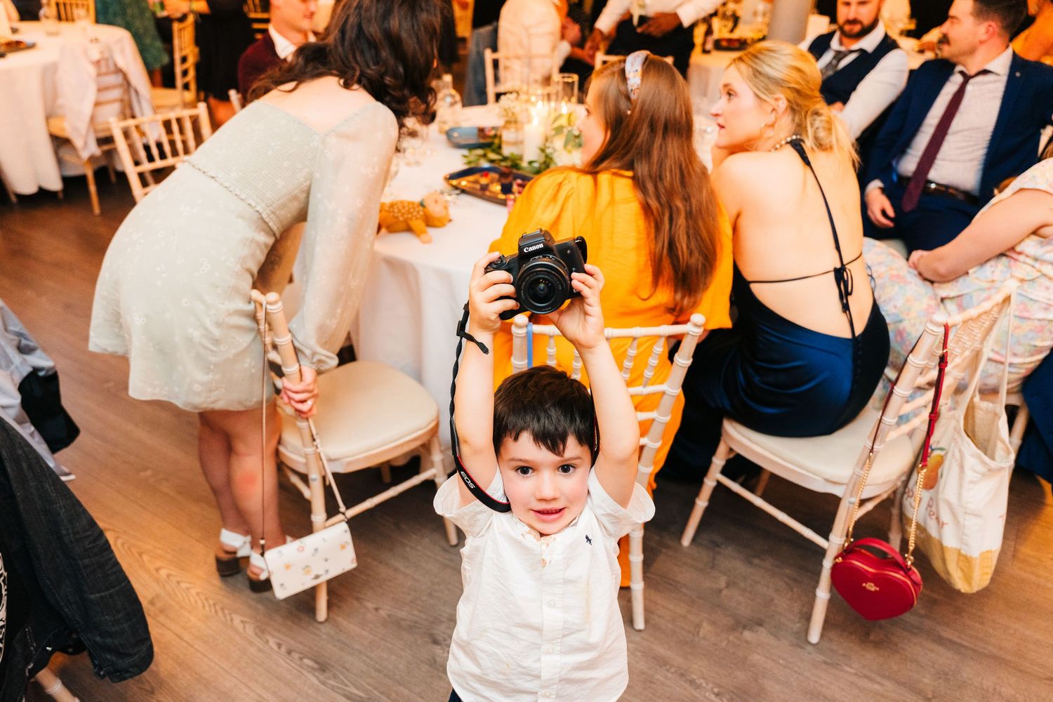 Young boy in white dress shirt dances at a wedding reception surrounded by seated guests. PHOTOGRAPHER Dublin Ireland Wedding