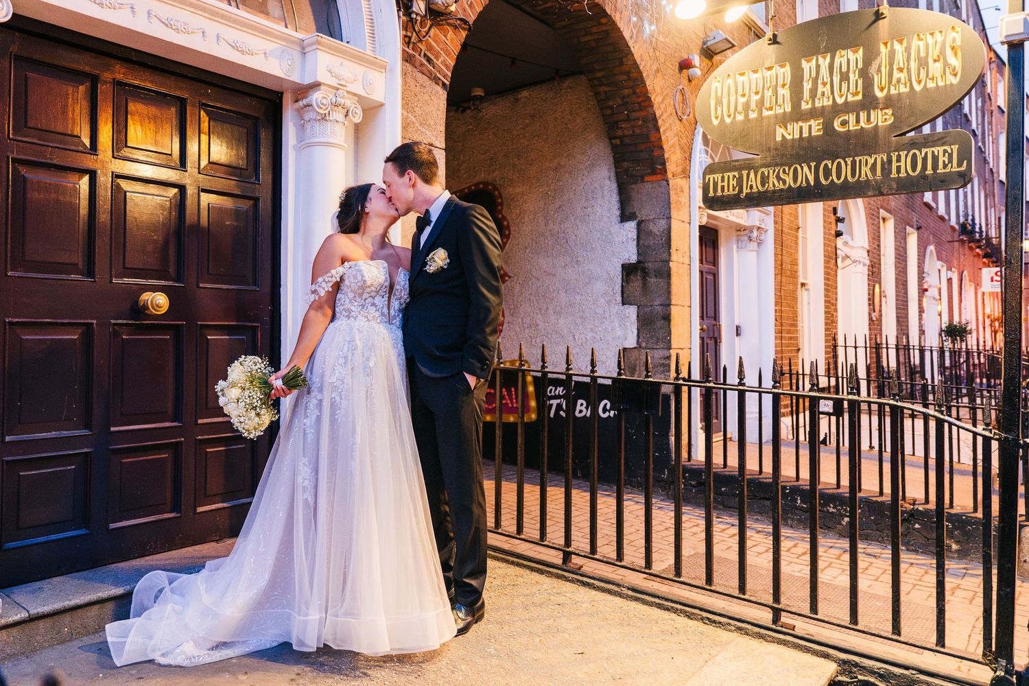 A couple poses in formal attire outside a historic London hotel entrance with iron railings. Wedding PHOTOGRAPHER Dublin