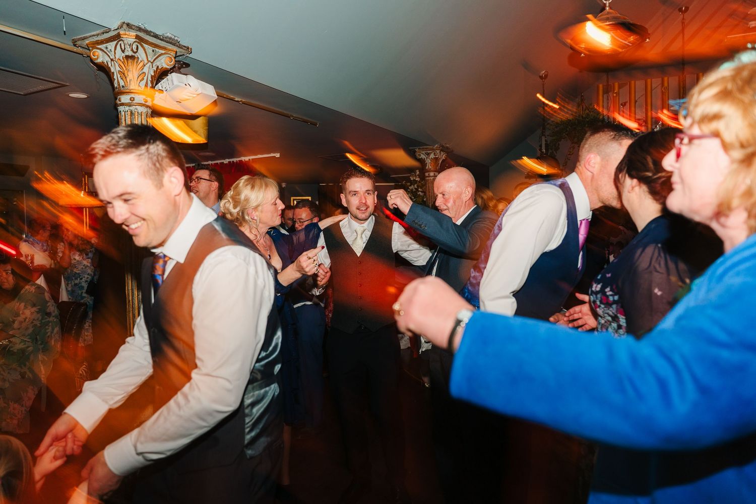 Dynamic party atmosphere with guests dancing under warm lighting at a reception. Marco Pierre Dublin Wedding Photographer