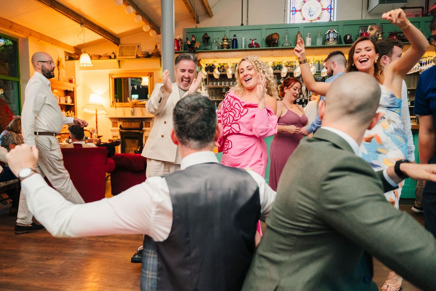Wedding guests dance and celebrate on a wooden dance floor under warm lighting. . Village Barn Tyrrellspass wedding photographer Ireland