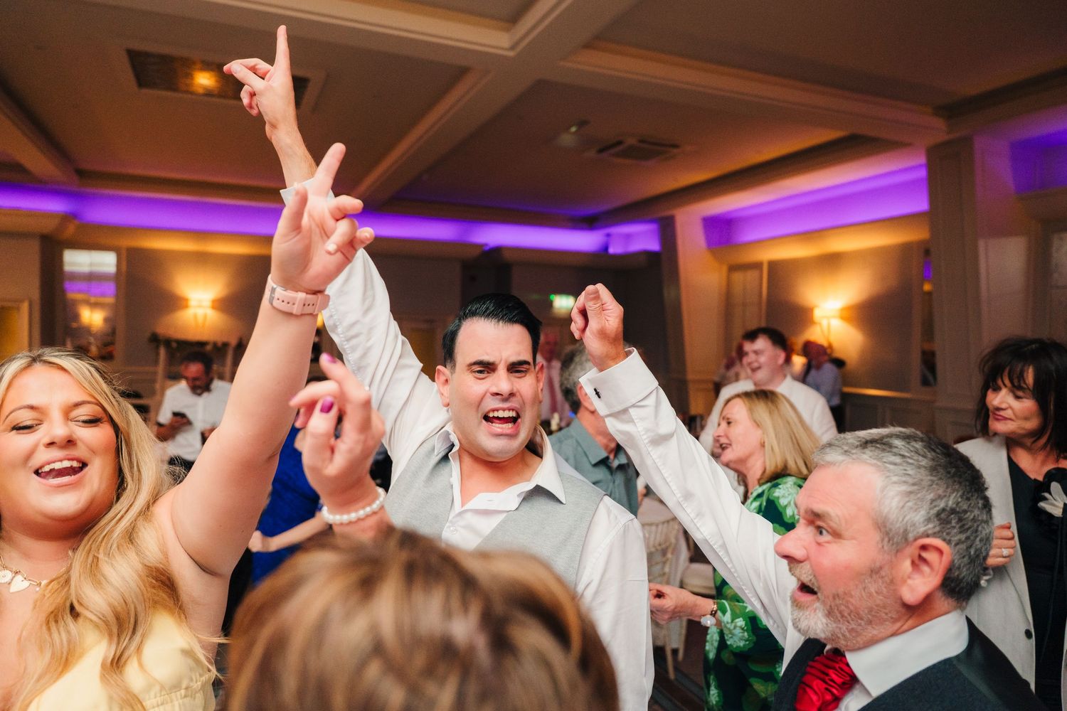 Wedding party guests dancing with hands in the air during lively reception celebration. Portmarnock Hotel Wedding PHOTOGRAPHER Dublin