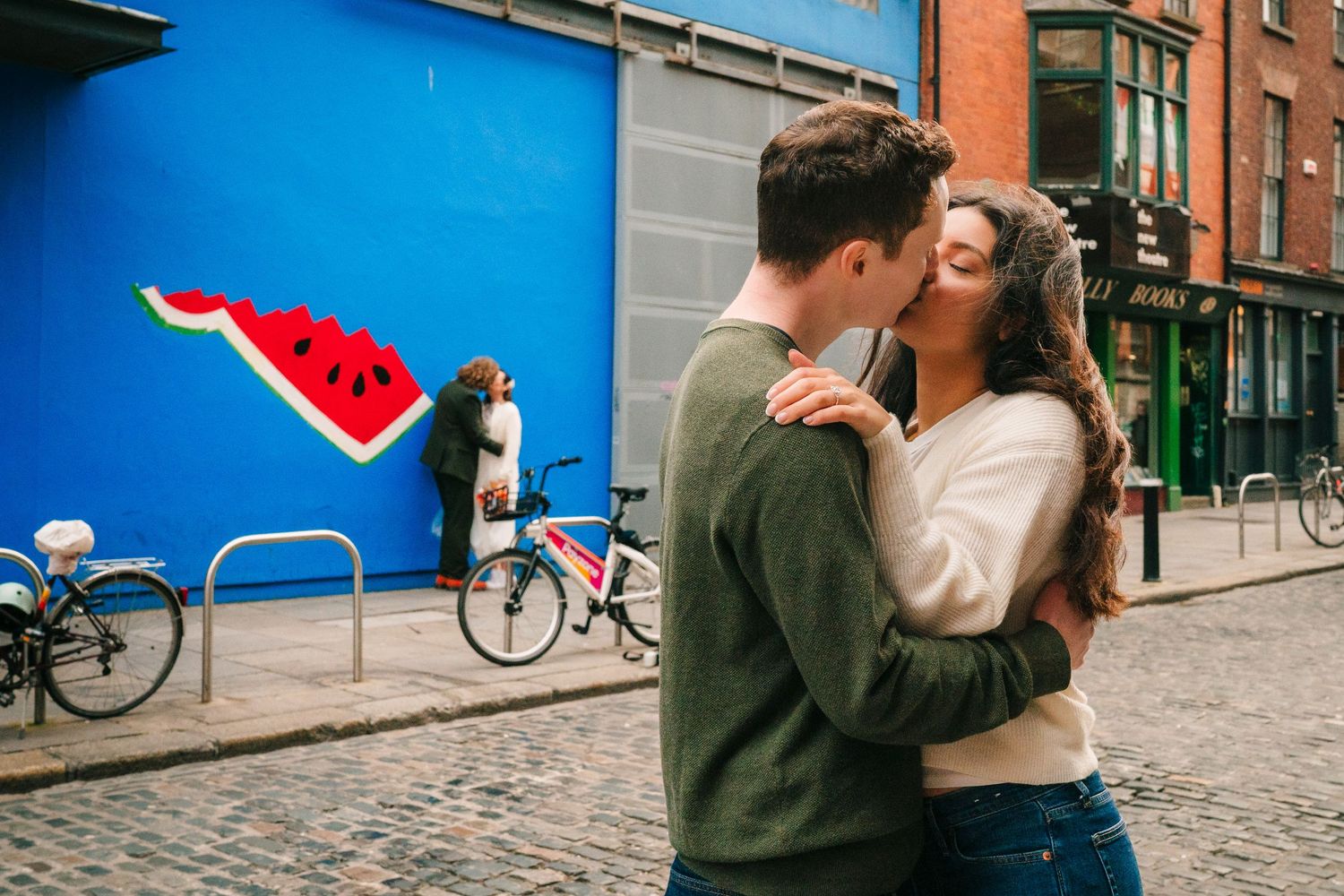 Couple sharing a romantic moment on a cobblestone street with blue wall and bicycle in background. Surprise proposal dublin photography