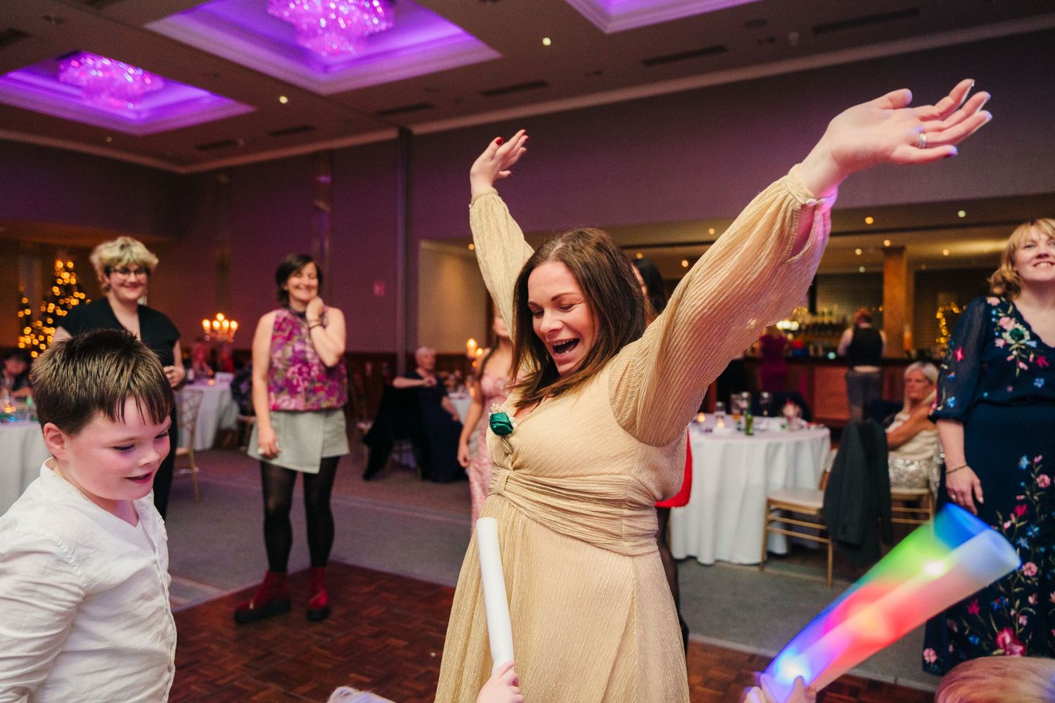 People dancing and celebrating at a wedding reception with purple lighting and colorful decorations.  Wedding PHOTOGRAPHER Trim Castle