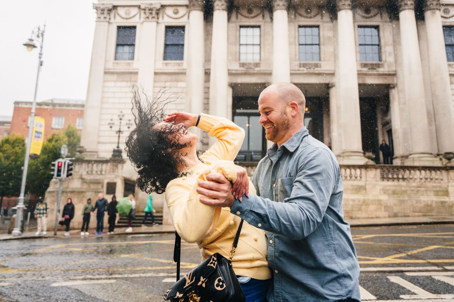 A couple shares a romantic moment outside a grand stone building with classical architecture on a cloudy day. Proposal Dublin Photographer