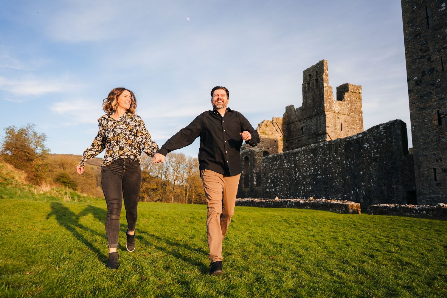 Playful couple running and jumping near stone castle walls during outdoor photo session. Photographer Ireland dublin
