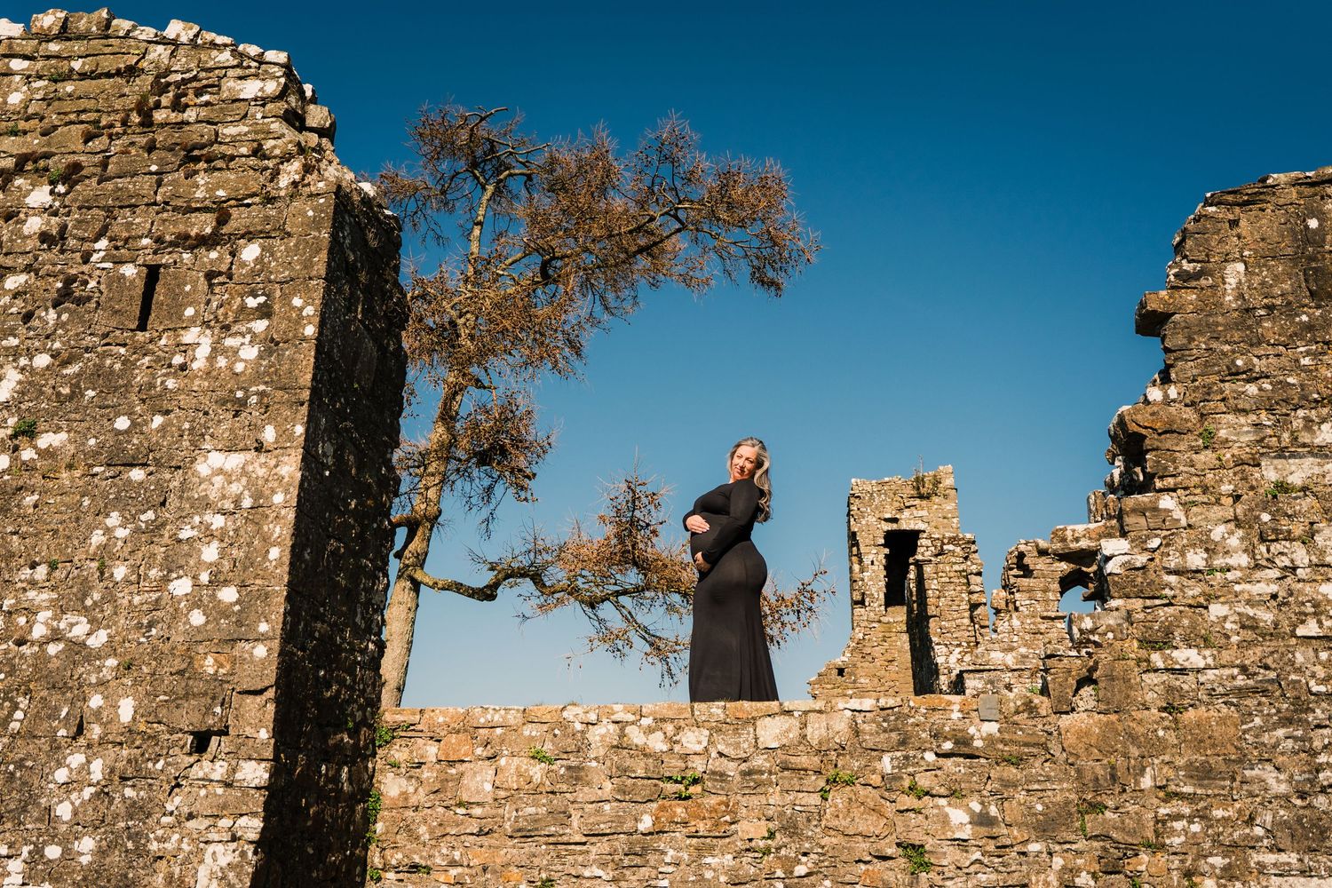 A silhouette stands atop ancient castle ruins against a bright blue sky. Family PHOTOGRAPHER Dublin
