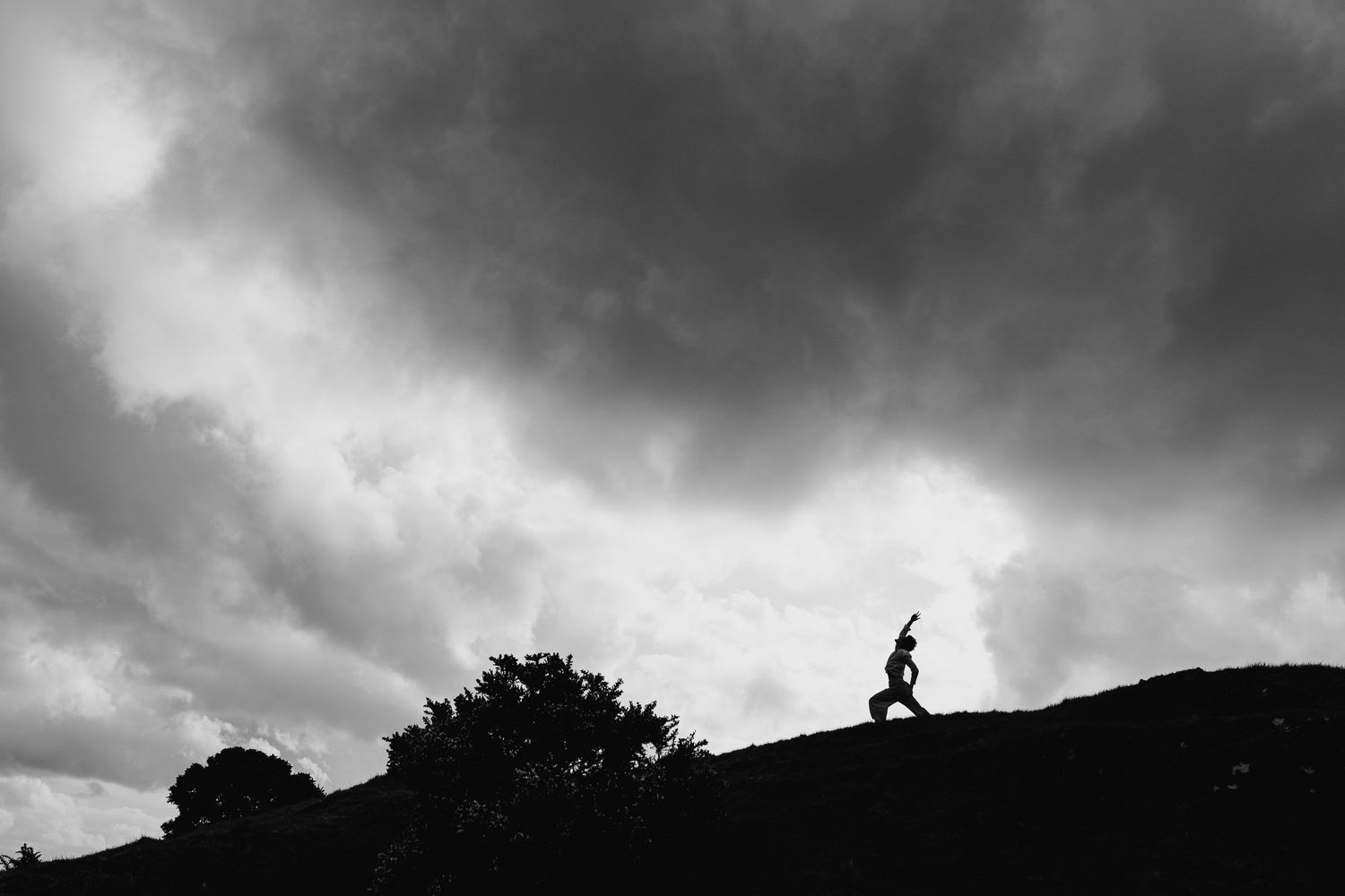 A lone silhouetted figure runs along a hilltop ridge against dramatic stormy clouds at dusk. Portrait PHOTOGRAPHER Dublin