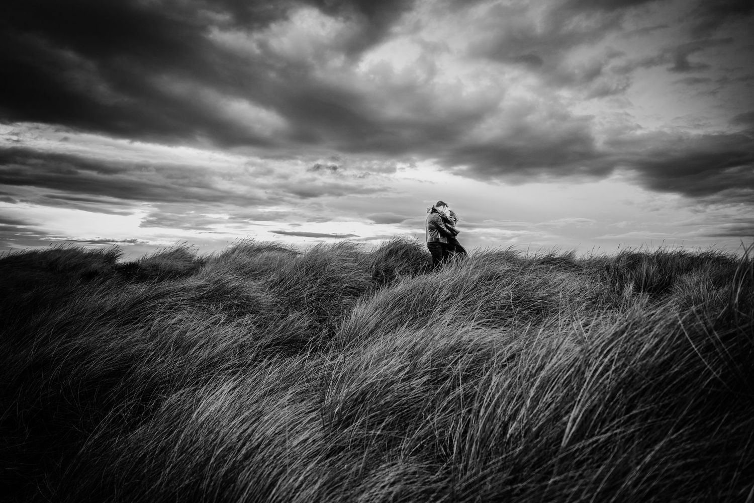 Dramatic black and white panoramic view of figures in windswept coastal dunes. engagement PHOTOGRAPHER Dublin