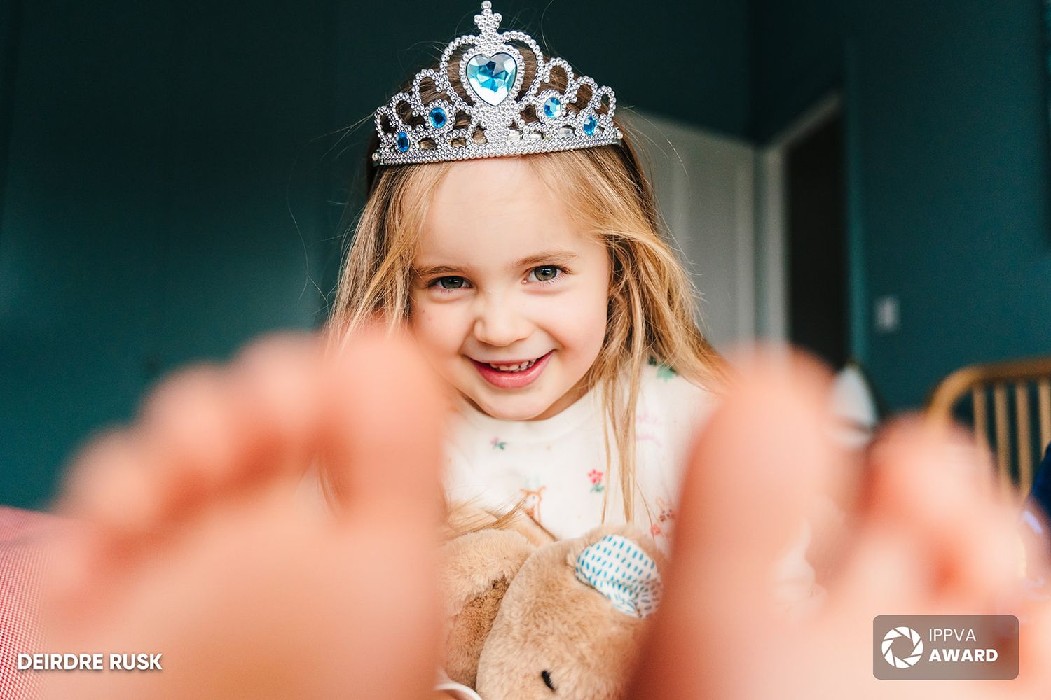 Young child wearing a sparkly princess tiara crown and white collar dress.