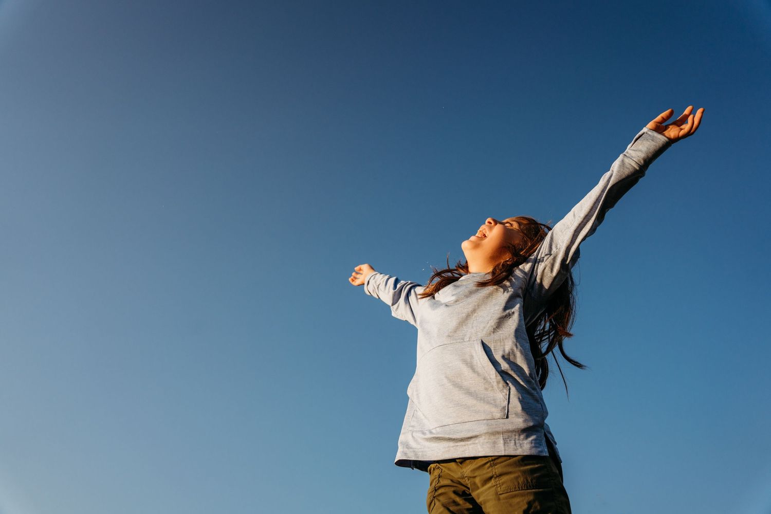 Figure stands against bright blue sky stretching arms up in joyful celebration pose. family PHOTOGRAPHER Dublin