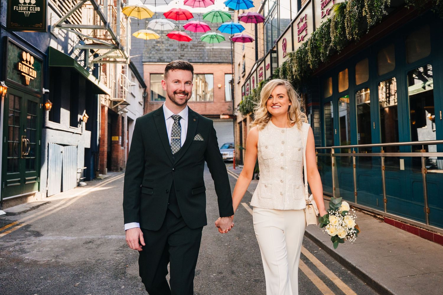 Couple walking down a bustling Dublin street with vibrant storefronts and pedestrians in view. City Hall Dublin wedding photogrAPher