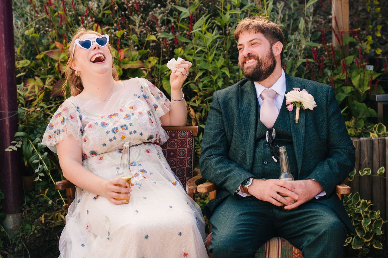 Wedding party members laugh and chat while sitting on outdoor benches during a garden celebration. . Village Barn Tyrrellspass wedding photo