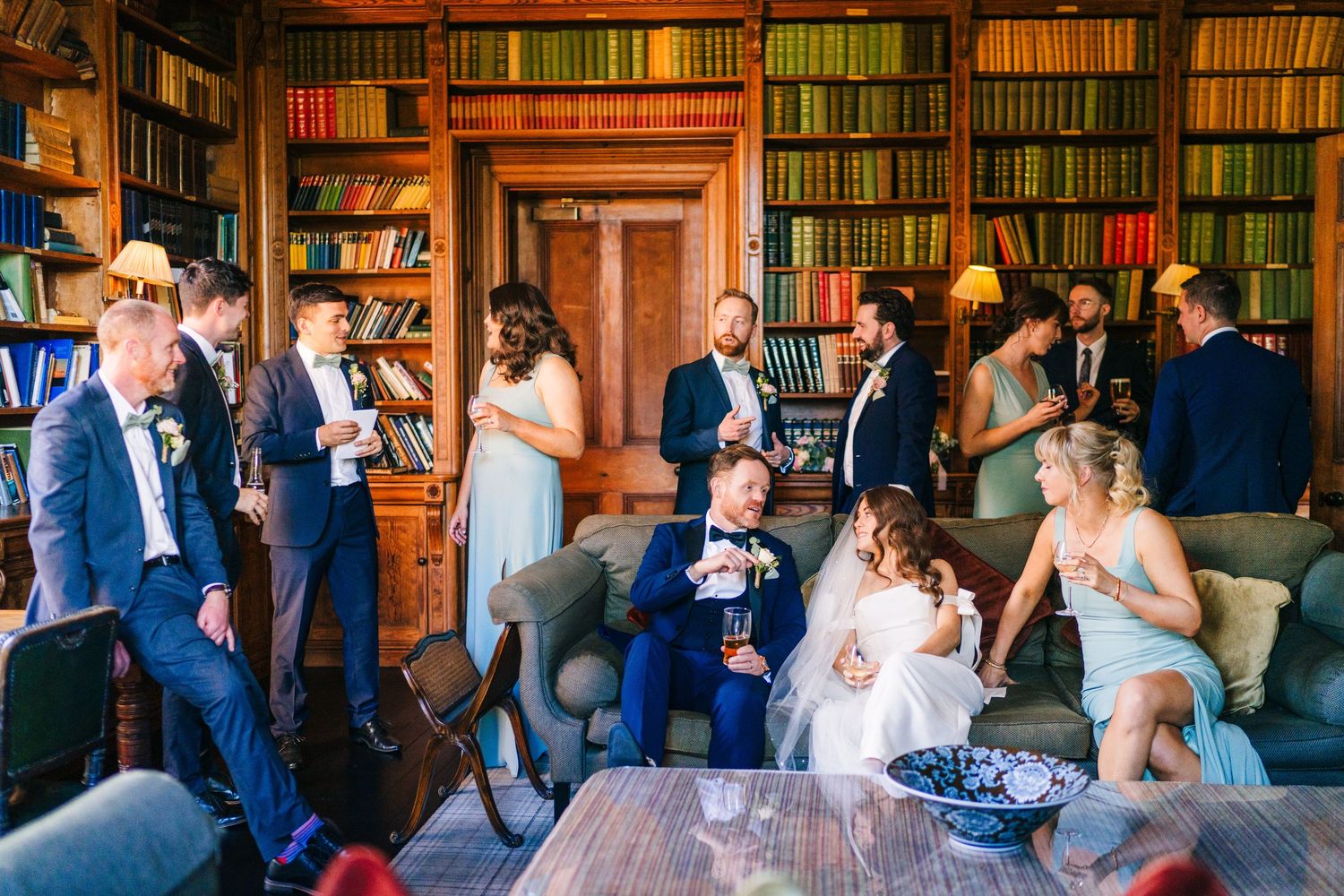 Castle Leslie Wedding Photographer DublA group enjoying a casual gathering in a classic wood-paneled library with wall-to-wall bookshelves.