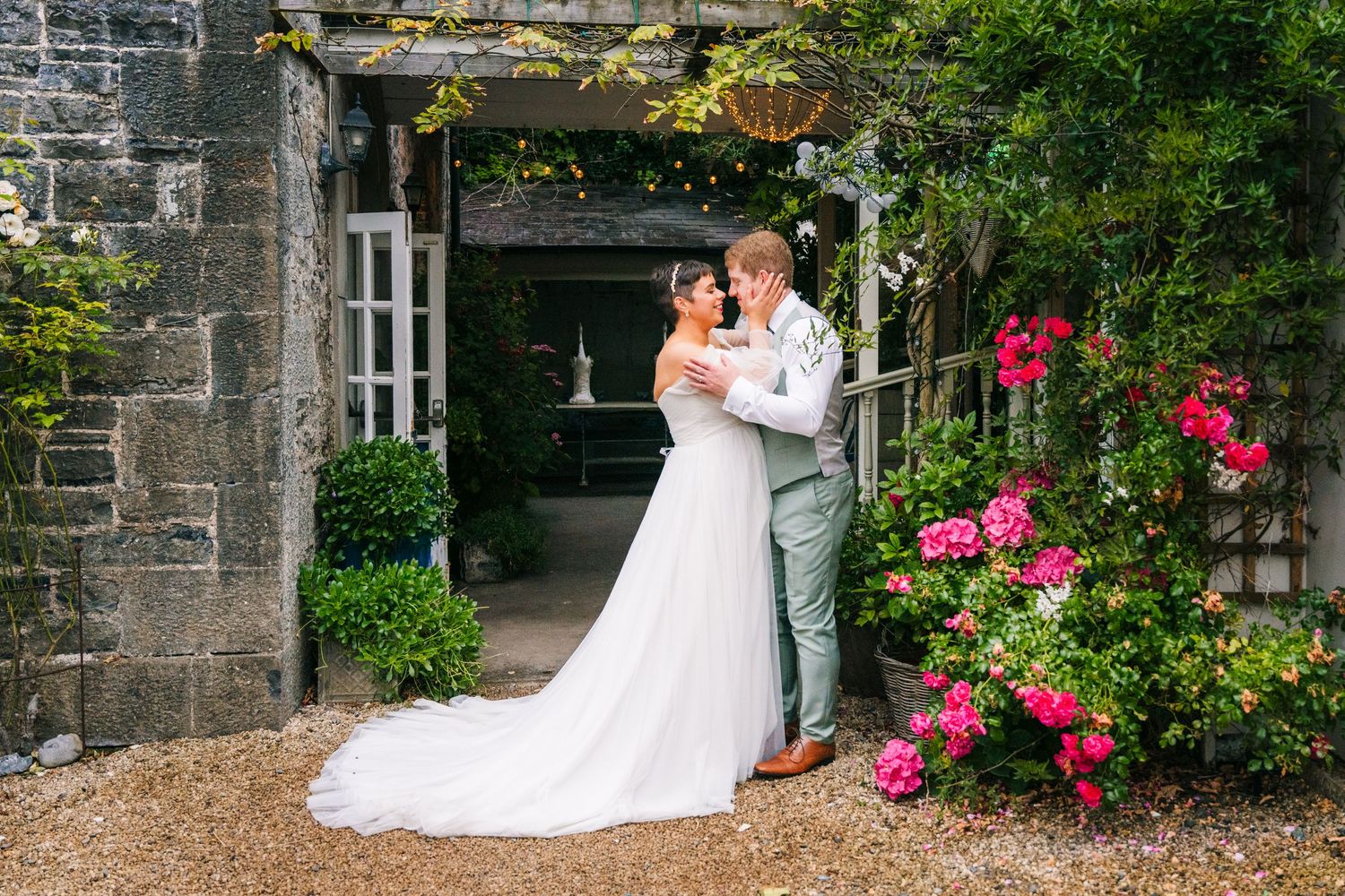 Millhouse slane wedA romantic wedding photo series featuring couples posing against stone walls with vibrant pink roses in a garden setting.