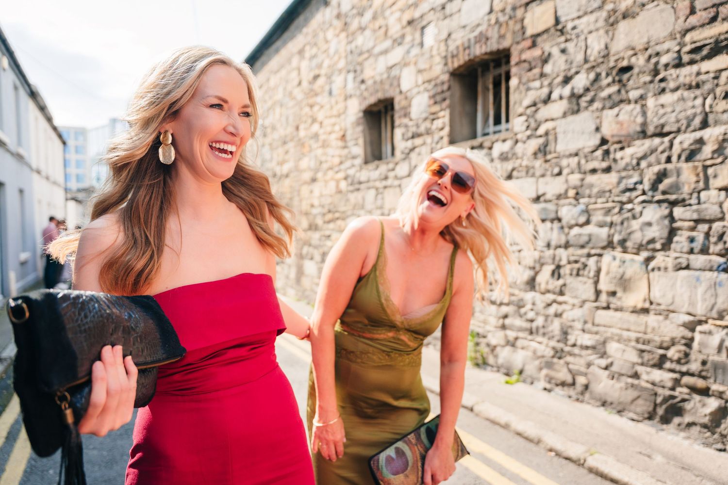 Wedding guests laughing and walking along stone wall on sunny day. Same sex wedding PHOTOGRAPHER Dublin