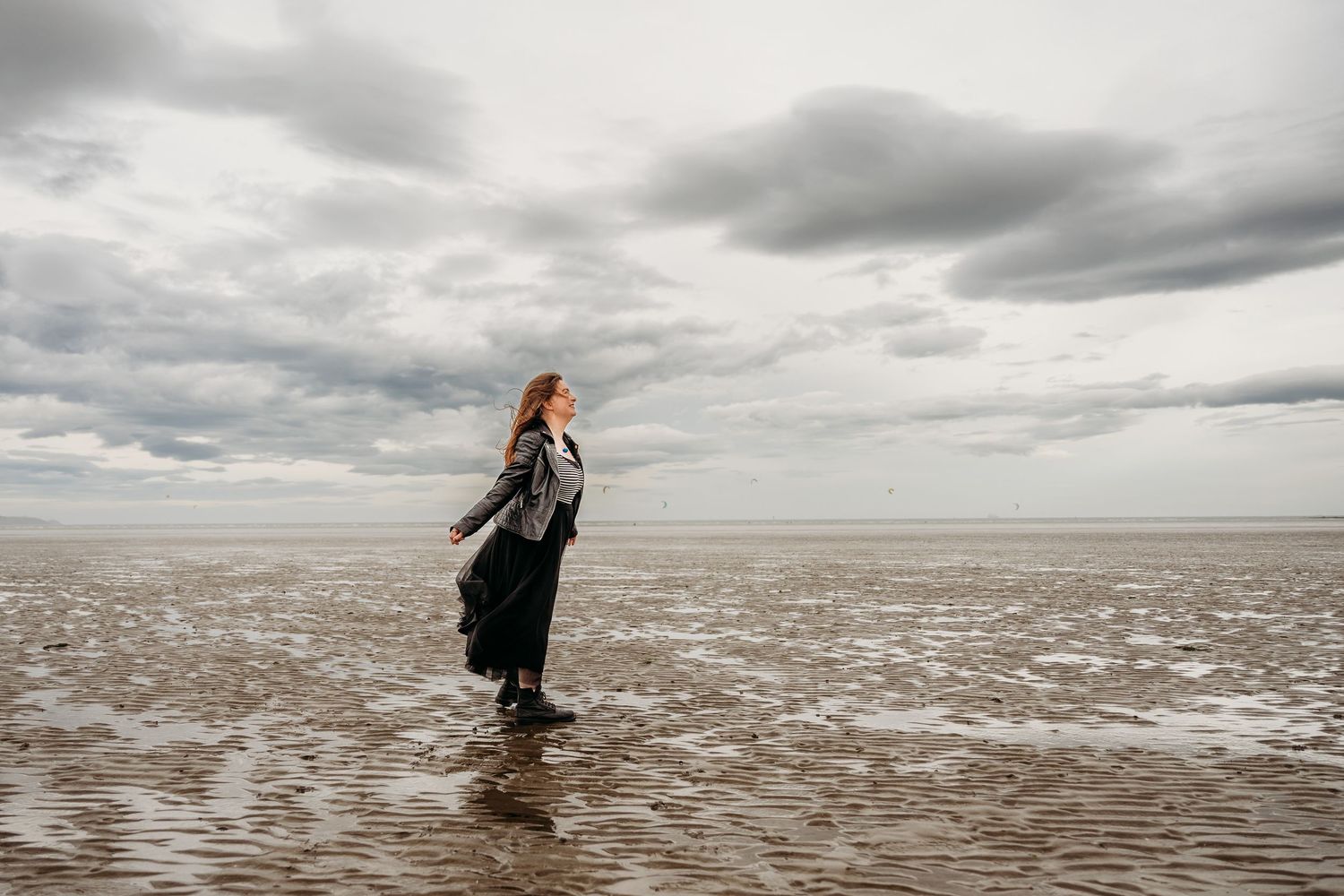 Panoramic beach scenes capture silhouettes moving across vast tidal flats under stormy gray skies. engagement PHOTOGRAPHER Dublin