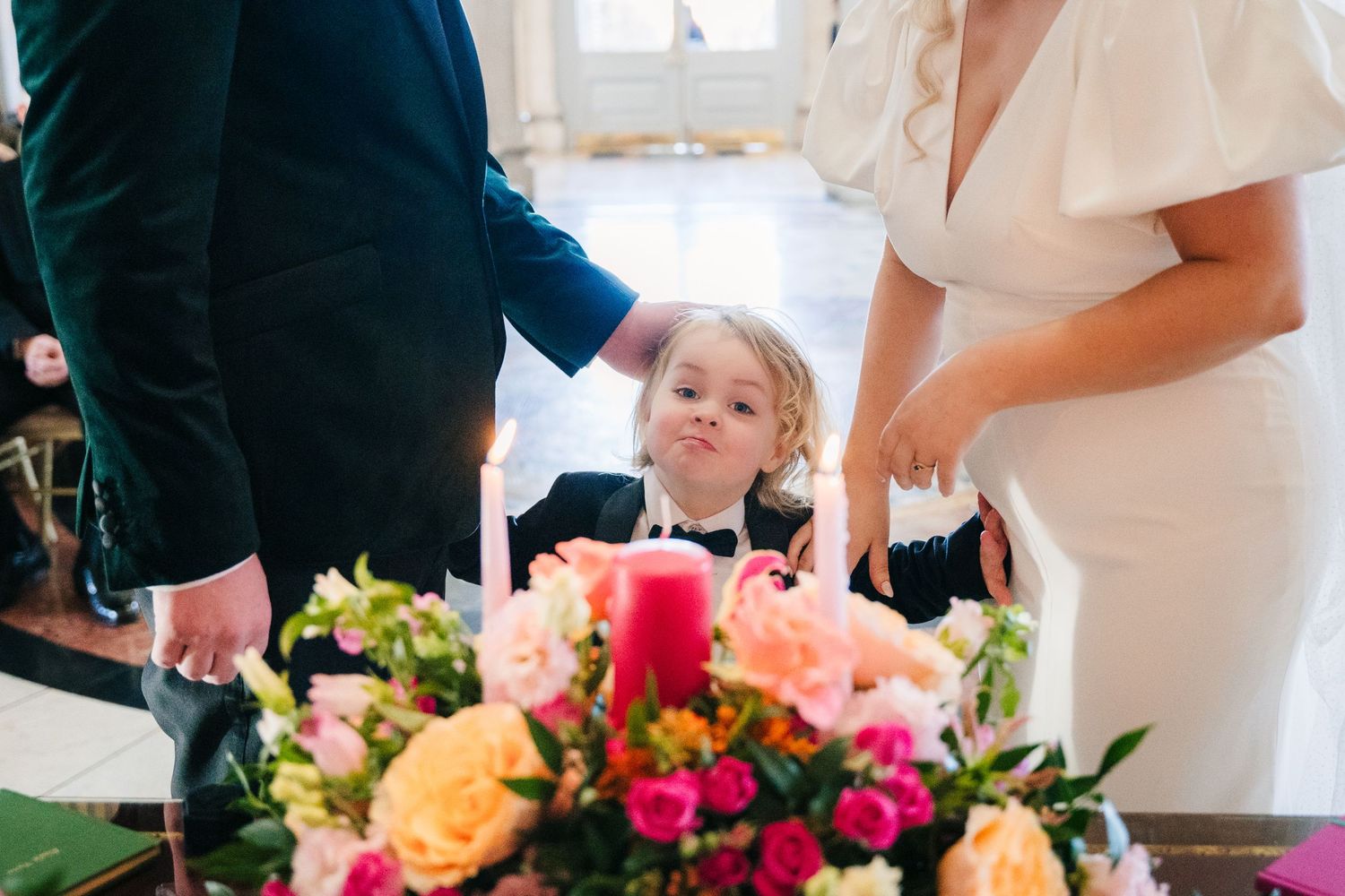 A child blows out a red candle at a wedding celebration with bright floral centerpiece of pink and orange blooms. City Hall Dublin Photograp