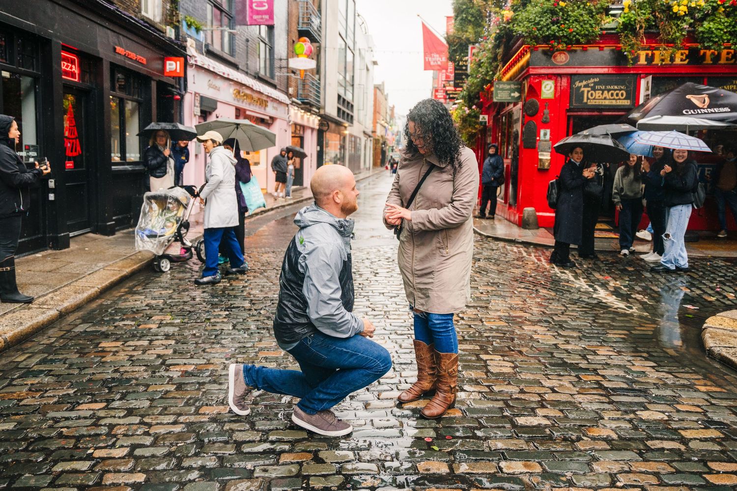 charming cobblestone street lined with bustling cafes and iconic red umbrellas on rainy day Proposal Dublin Photographer