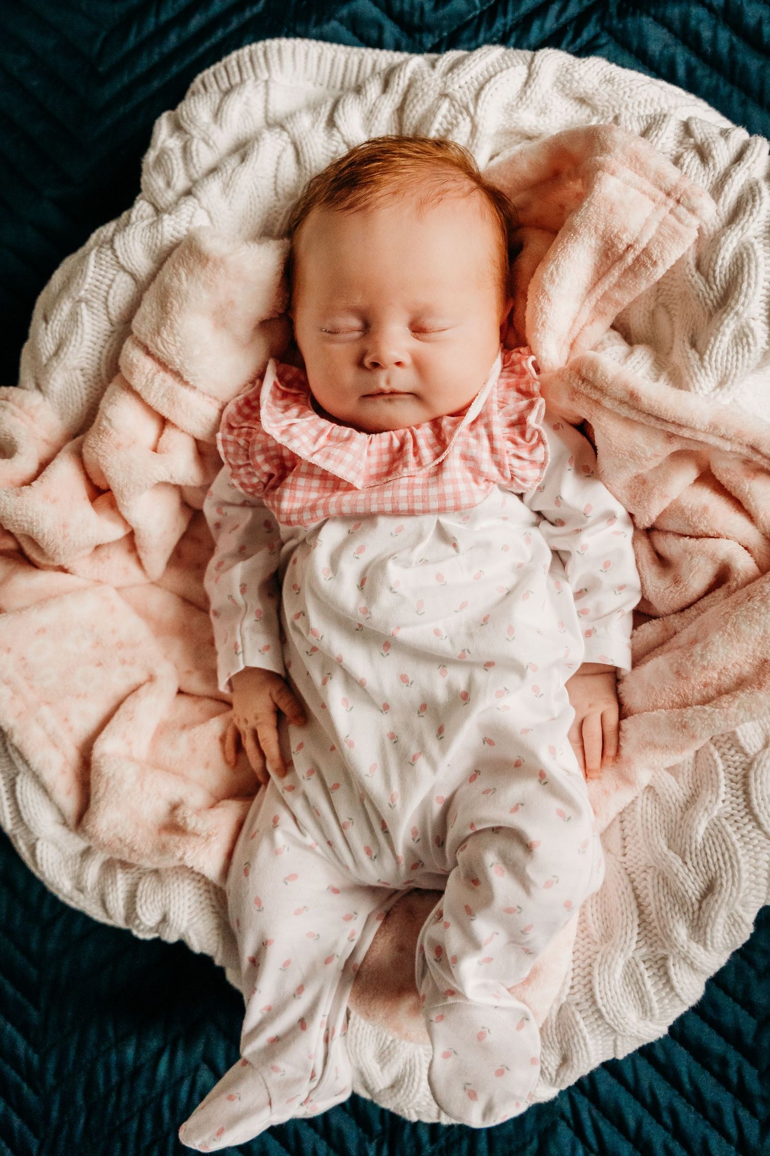 Sleeping newborn baby wearing pink and white clothing lies peacefully on soft cream blanket against dark blue background. Family PHOTOGRAPHE