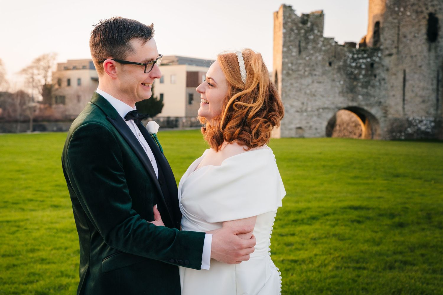 Couple embraces in front of a historic stone castle wall during sunset.  Wedding PHOTOGRAPHER Trim Castle