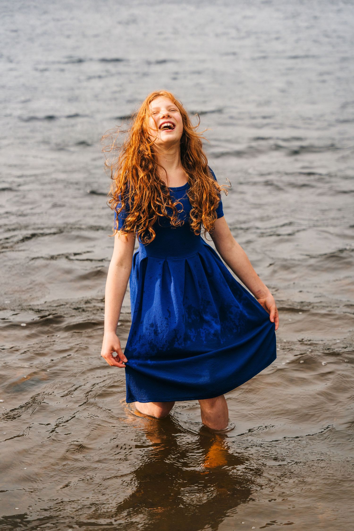 A joyful figure in a navy blue dress plays in the water at the beach, creating a carefree moment. Family photographer dublin