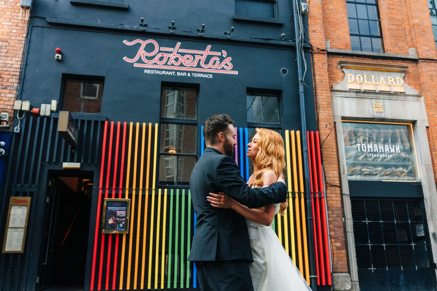 Wedding couple posing in front of a colorful striped wall with vintage signage and urban architecture.  city hall dublin wedding photos
