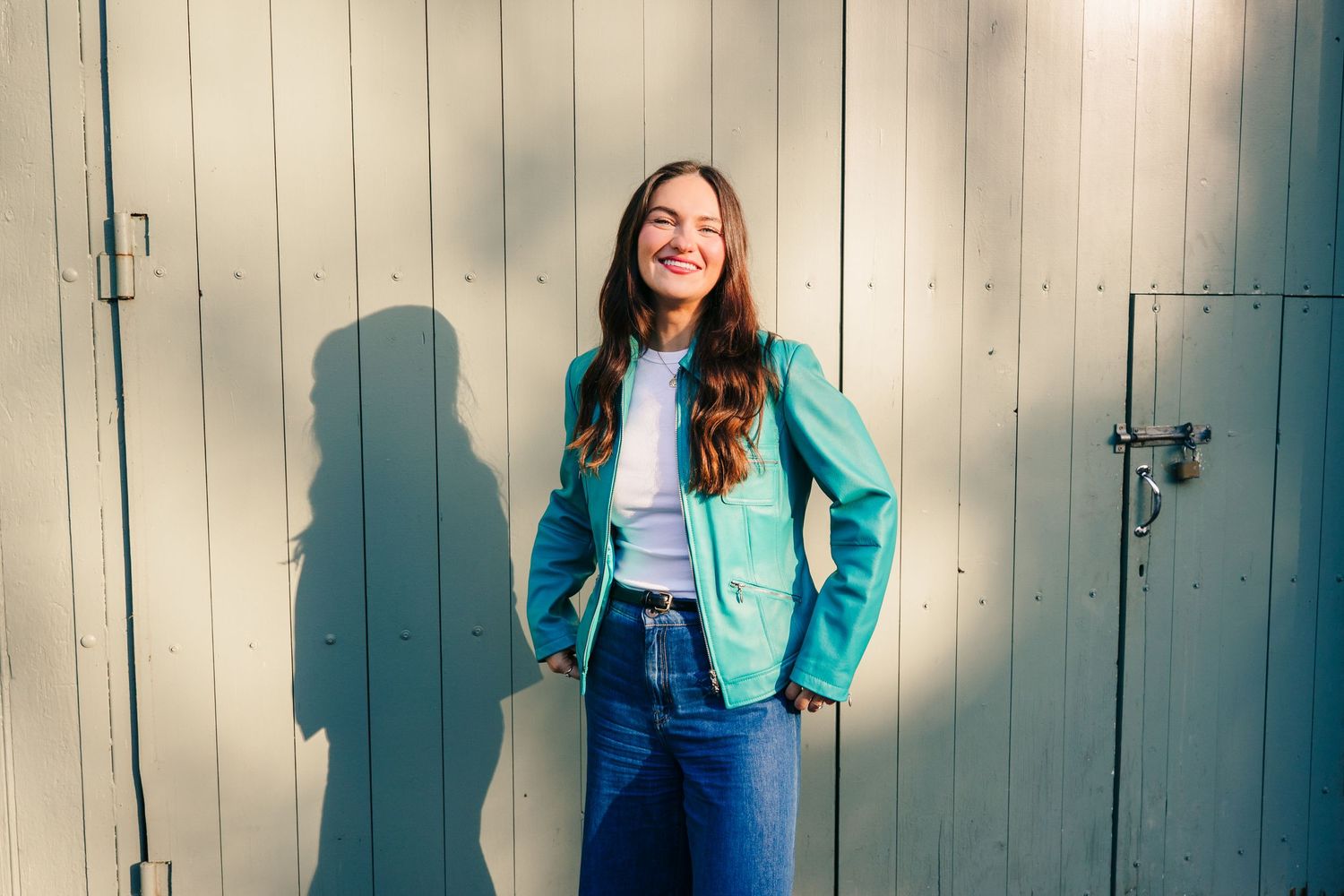 A person in a turquoise blazer and dark jeans poses against a rustic wooden wall with natural Dublin Professional headshots PHOTOGRAPHER
