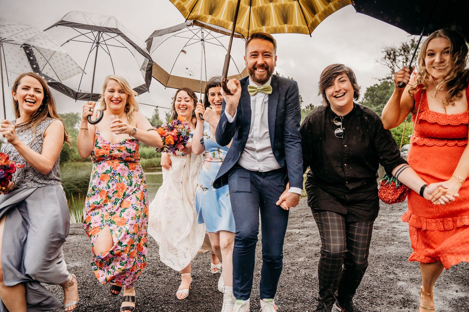 Wedding party celebrating with umbrellas outdoors in a candid group photo. Wedding photographer Dublin