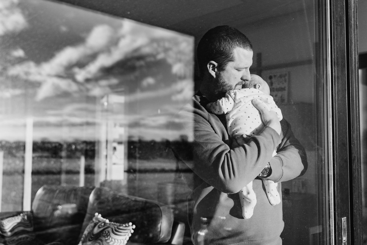 Black and white photo of parent holding infant while gazing out window with scenic view. family PHOTOGRAPHER Dublin