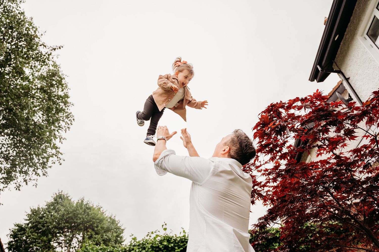 Person in white dress twirling joyfully outdoors with red maple trees and greenery in the background. family PHOTOGRAPHER Dublin