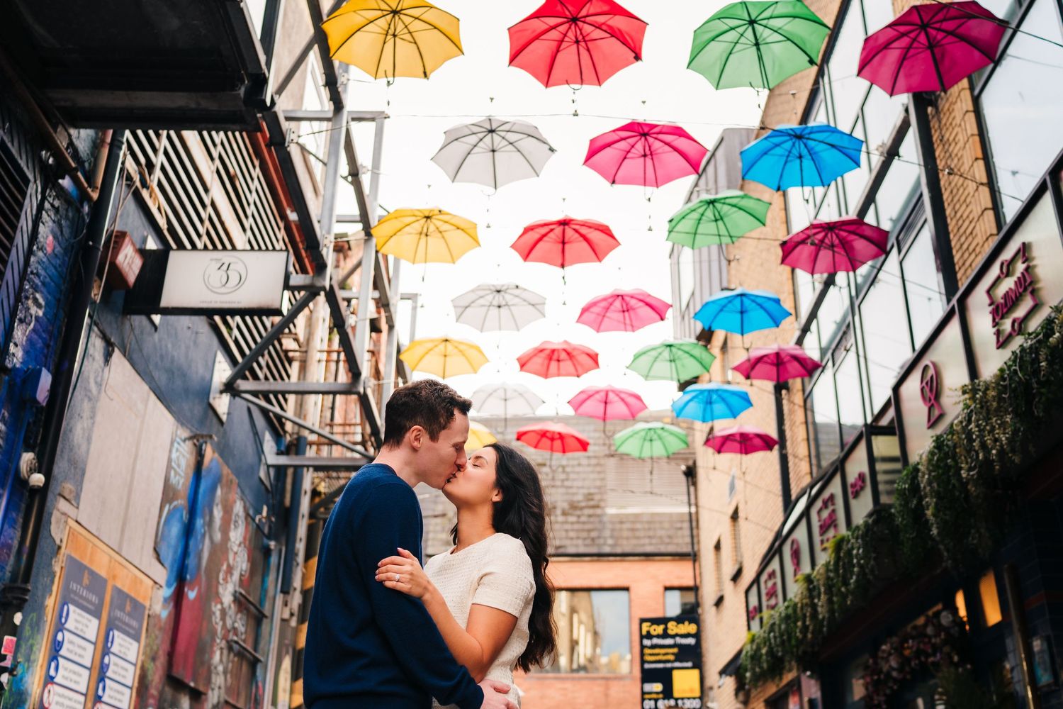Colorful umbrellas hanging overhead create a vibrant canopy above an urban street. PHOTOGRAPHER Dublin
