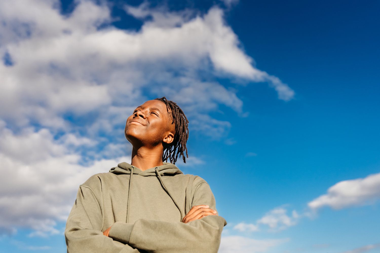 A person in a tan jacket gazes upward towards a bright blue sky with white puffy clouds on a sunny day. family PHOTOGRAPHER Dublin