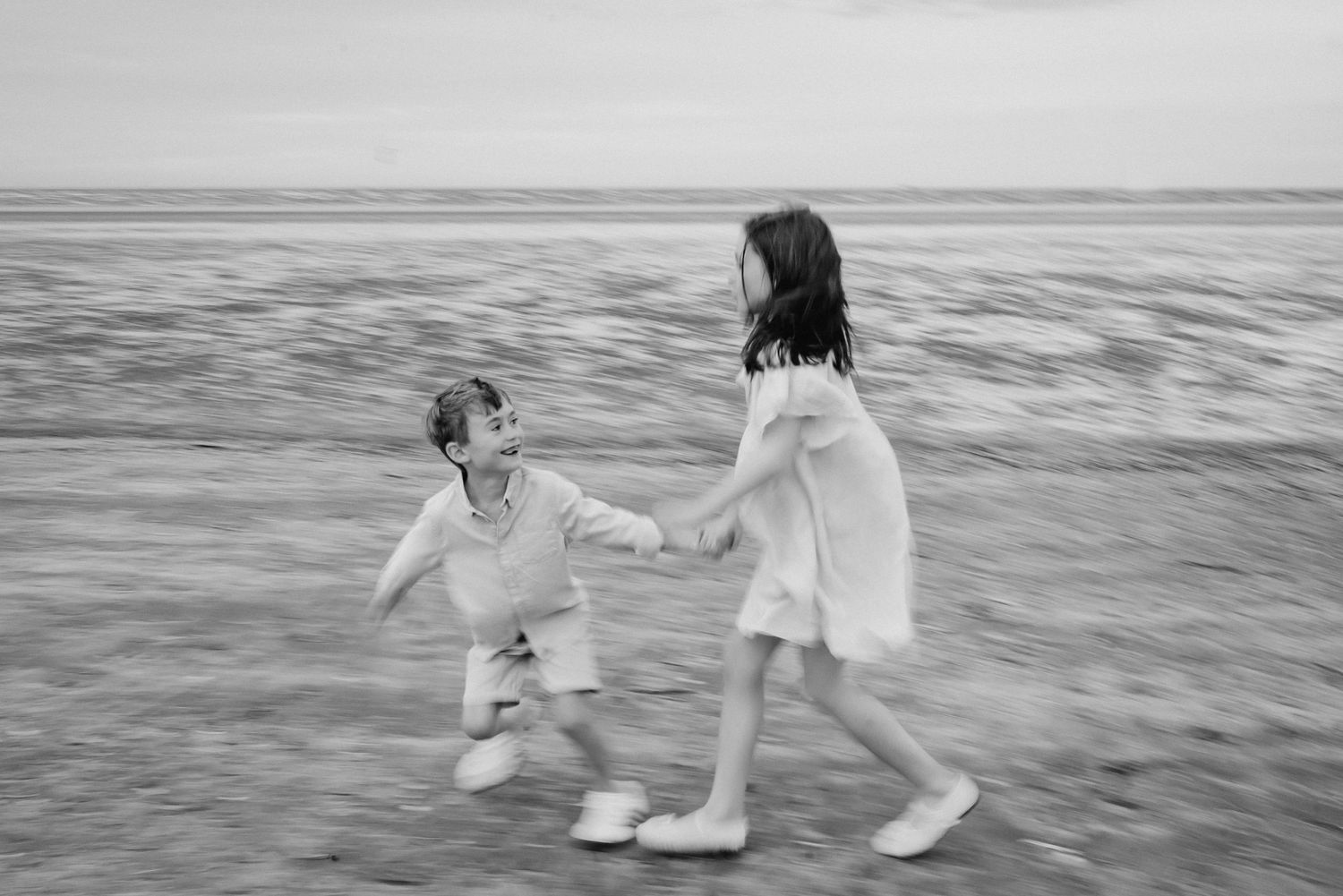 Black and white photo of two children playing and splashing in shallow water.  Family photographer Dublin Ireland