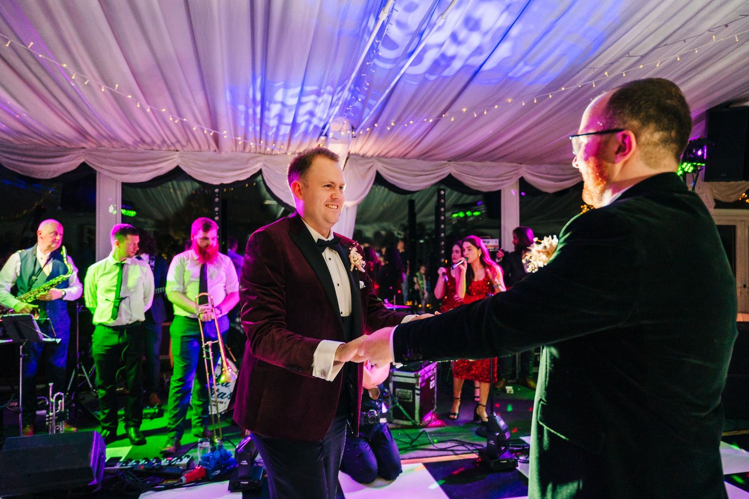 Wedding celebration with colorful purple lighting and guests dancing under a tent. LGBTQ Ashley Park Wedding Photographer