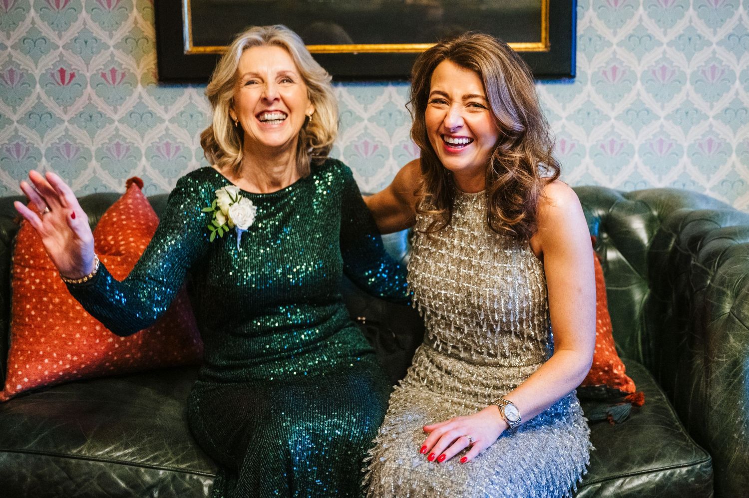 Two women in sparkly evening dresses share a joyful moment on a vintage couch.  Virginia Park Lodge Wedding Photographer Cavan Dublin Irelan